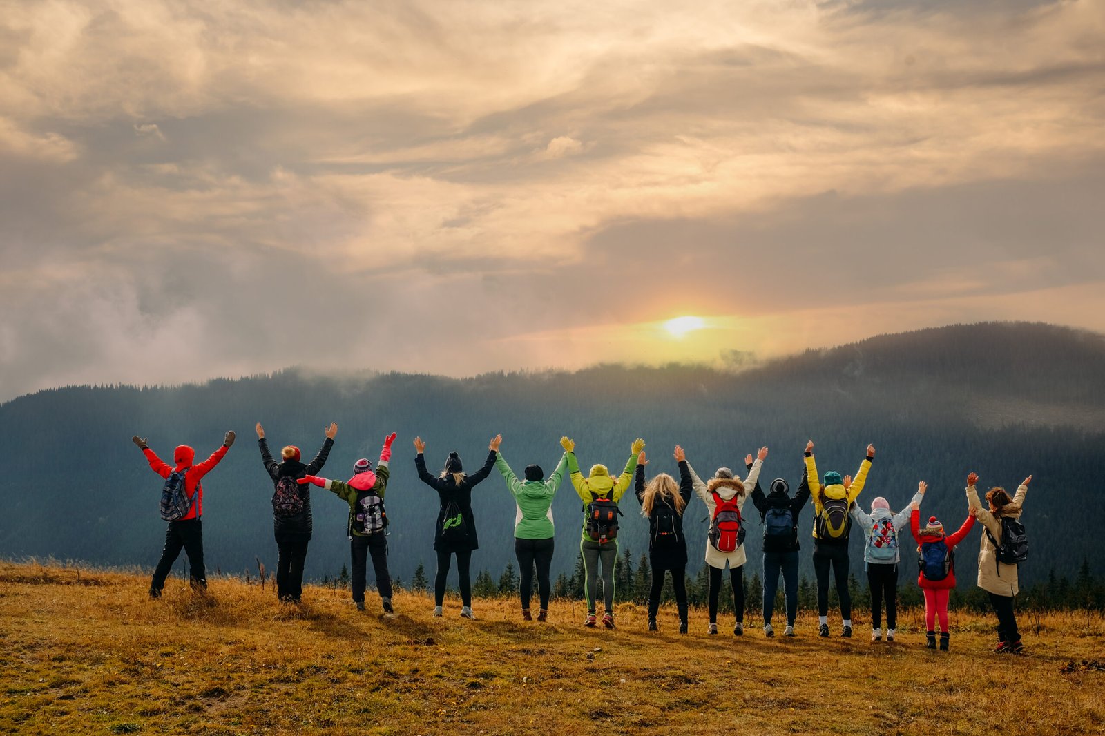 Big group of friends travel together and enjoy the mountain landscape at sunset with raised hands