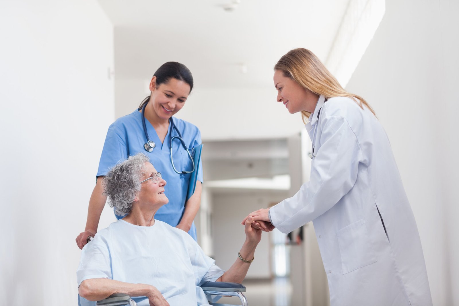 Patient in a wheelchair holding hand of a doctor in hospital ward